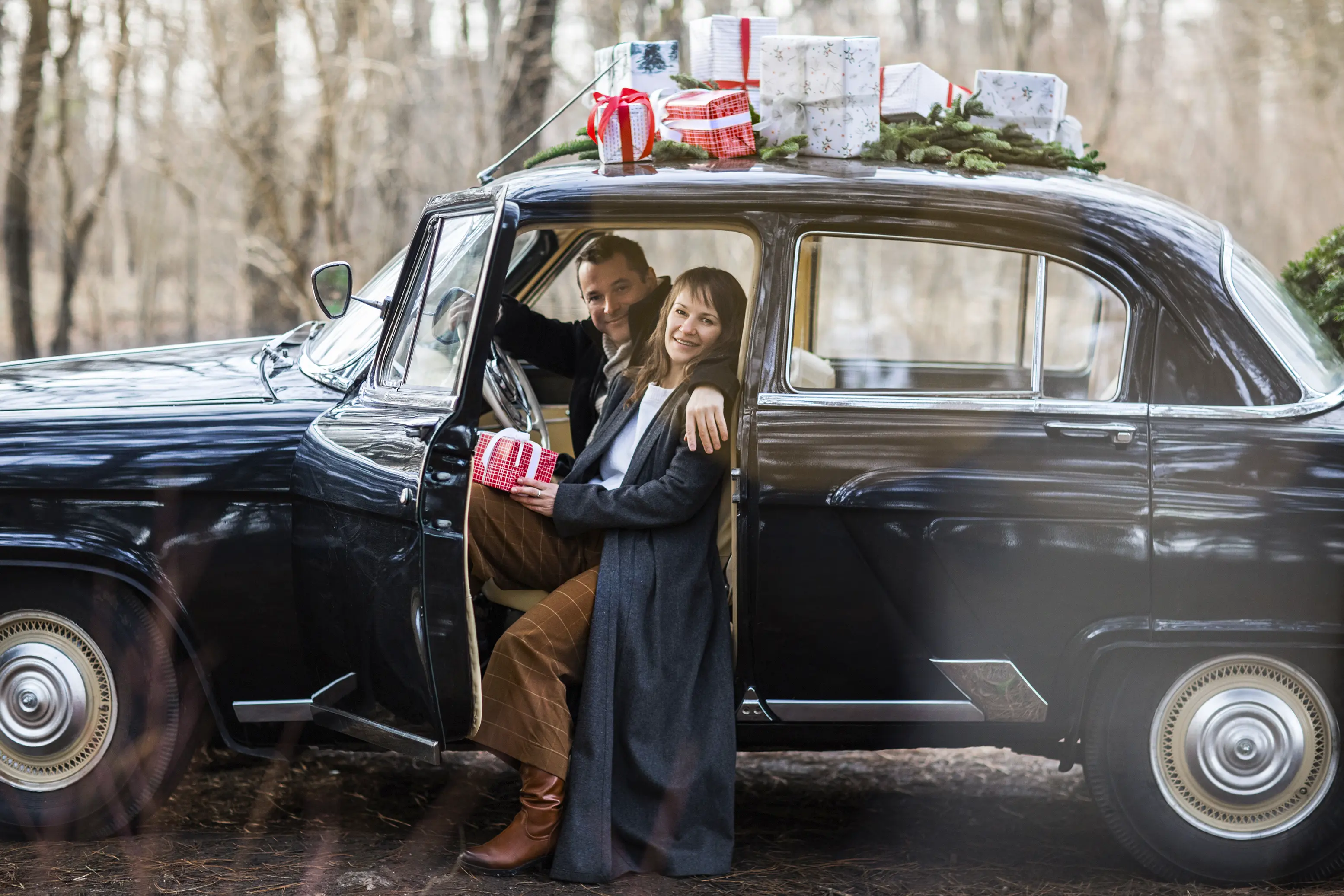 Couple sitting in a vintage car with Christmas gifts